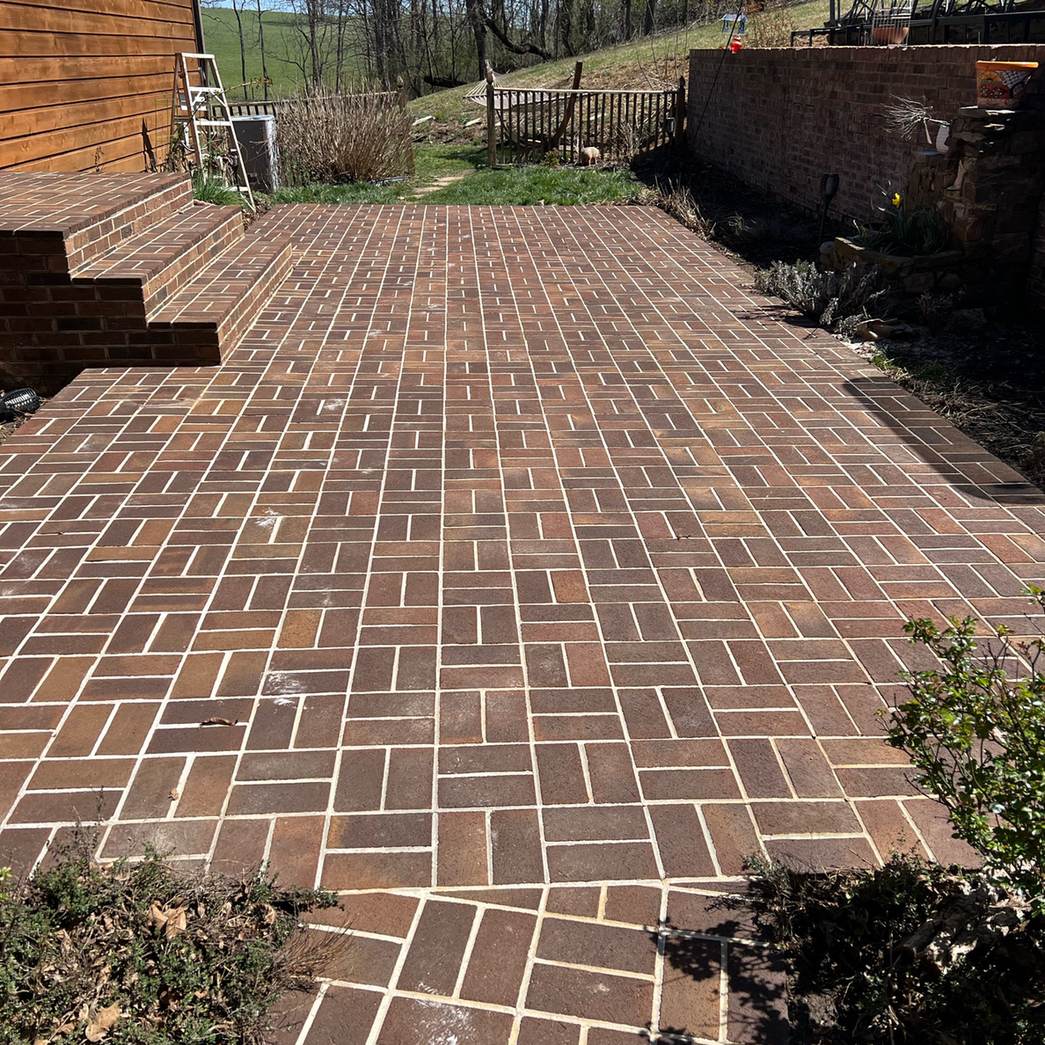 A red brick paver patio beside a stained deck, the brick bright after the clean
