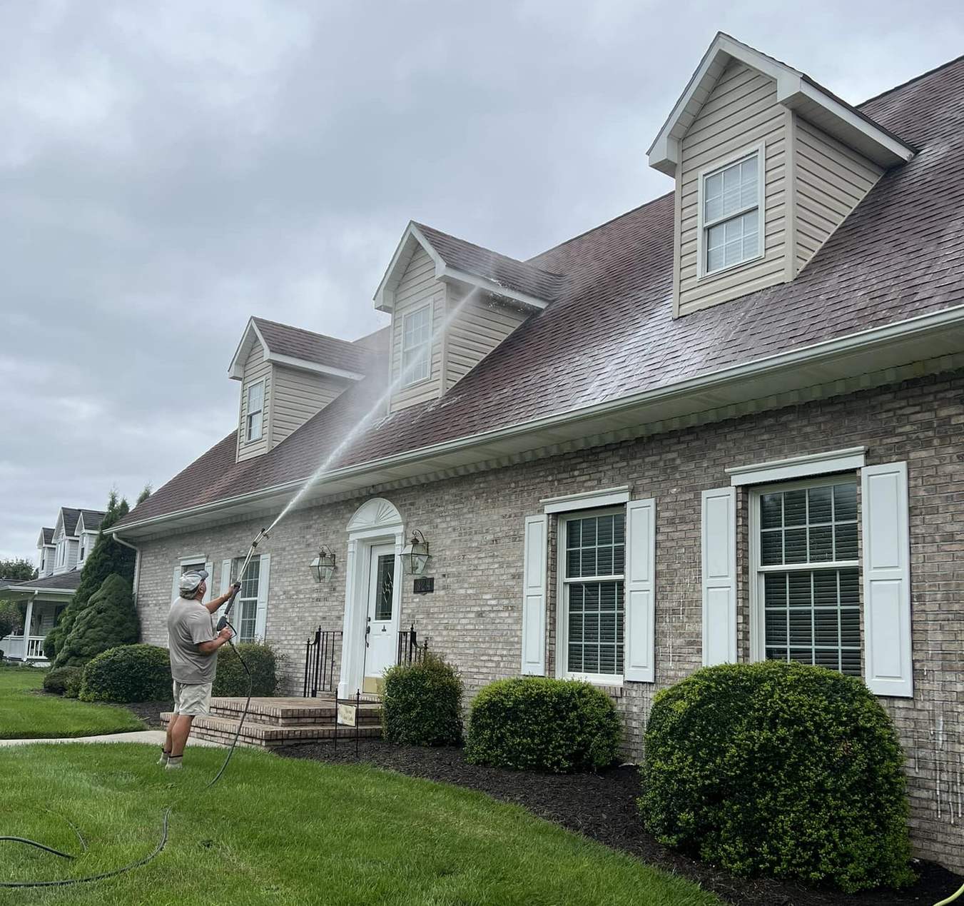 Washing the roof and siding of a cream and stone cape cod with dormers