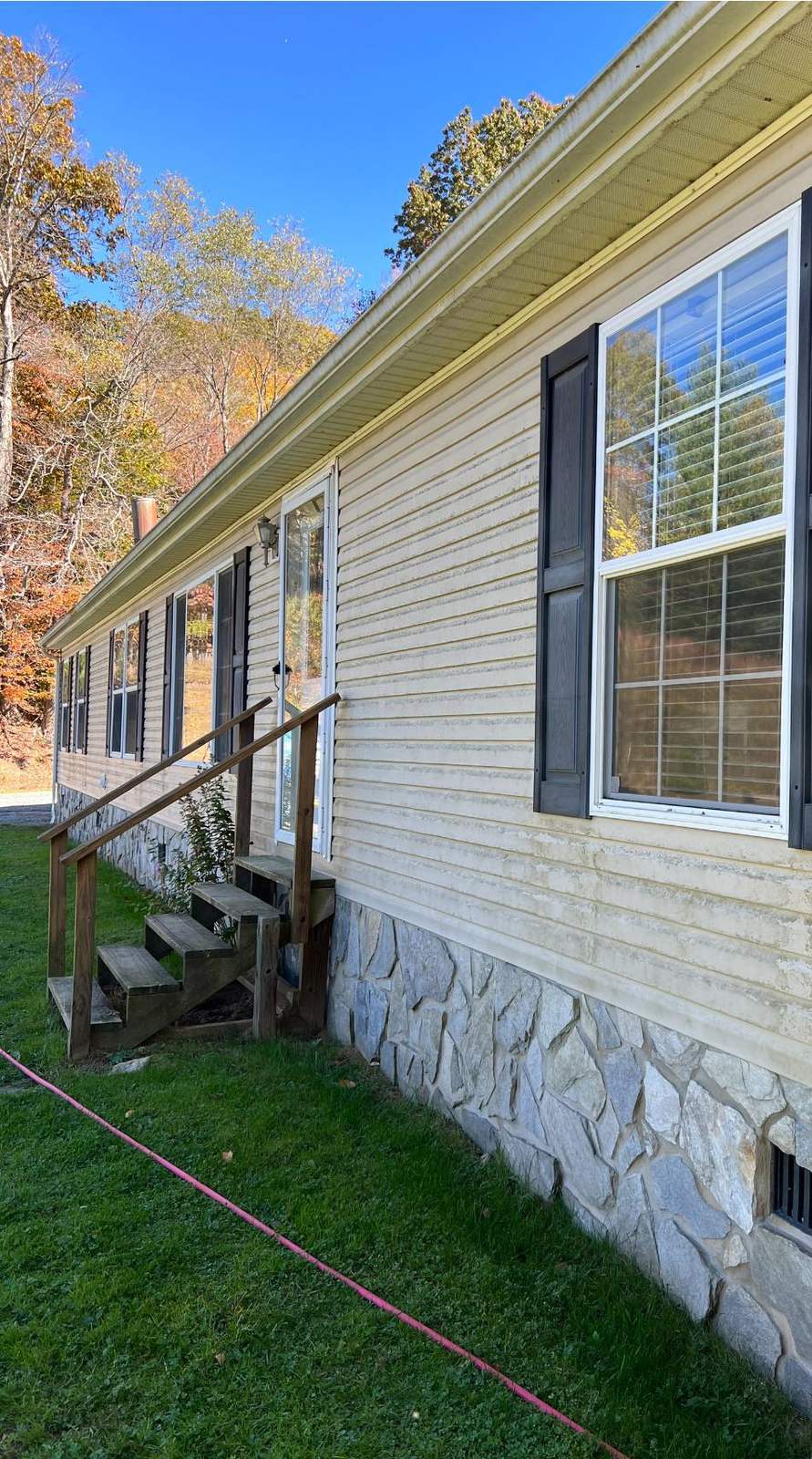 Cream vinyl siding before the wash, dingy and streaked above a stone skirt